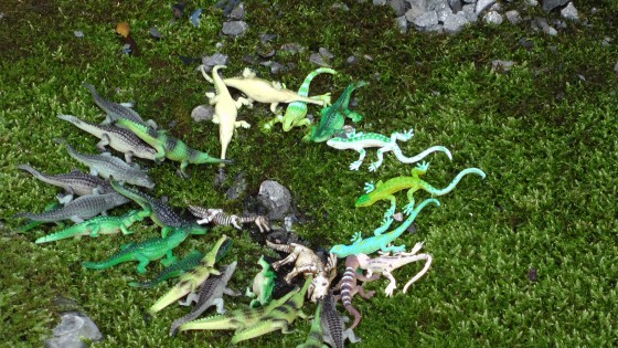 Some dollar store plastic crocodiles hanging around a rock.